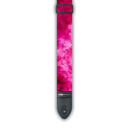 A pink watercolor patterned padded guitar strap with black ends and the brand name 'Riff Wraps' visible.